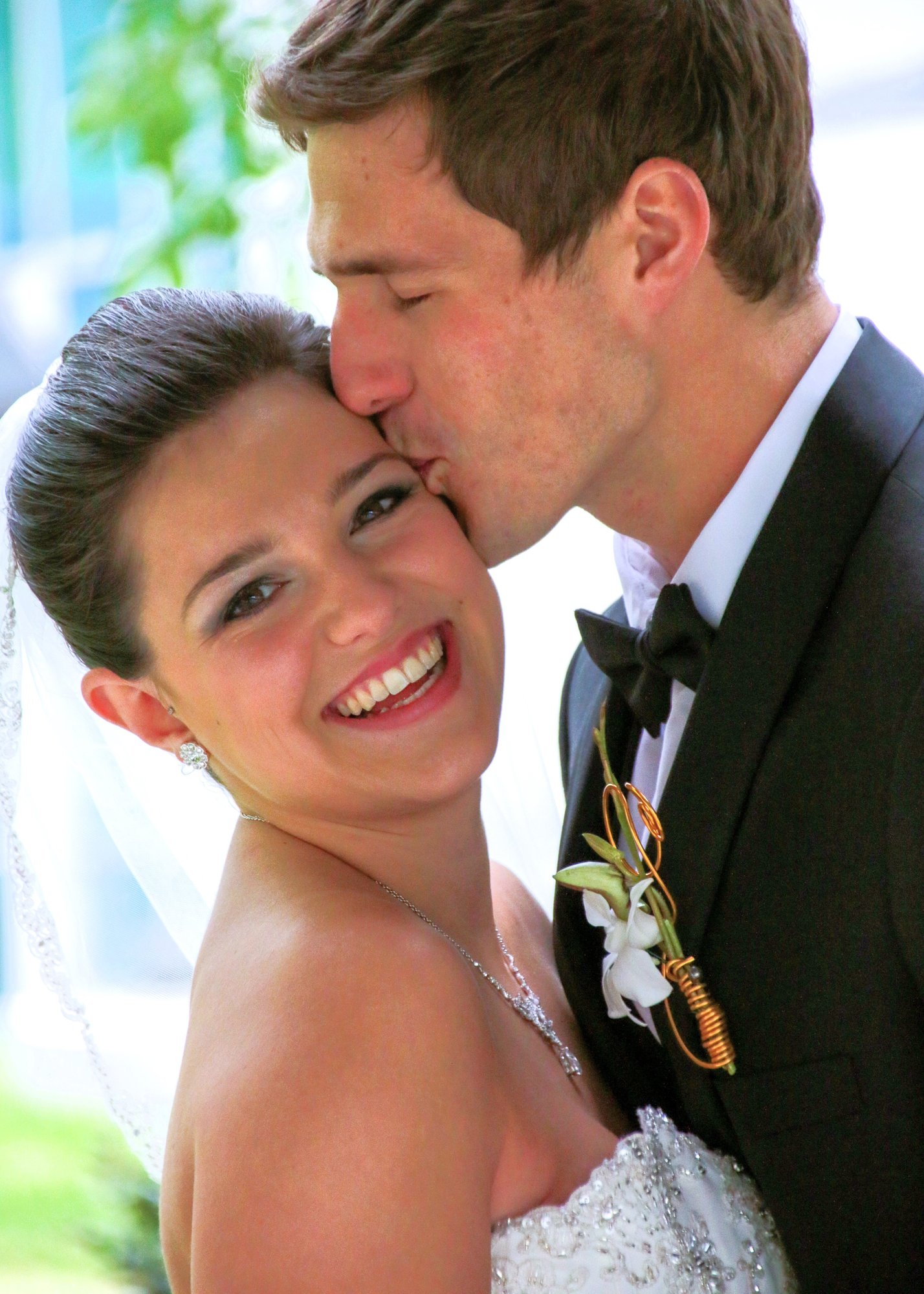 groom kissing smiling bride's temple