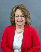 confident woman over 50 in a red suit with pearl necklace